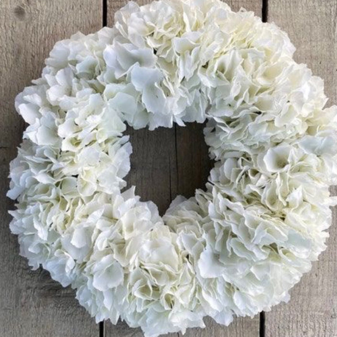 A white faux hydrangea wreath displayed on a rustic wooden plank background, with 'On Etsy now' text overlay at the top.